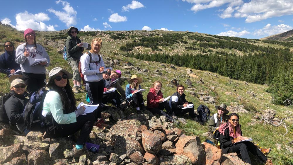 Group of students posing for a photo while sitting on a hillside