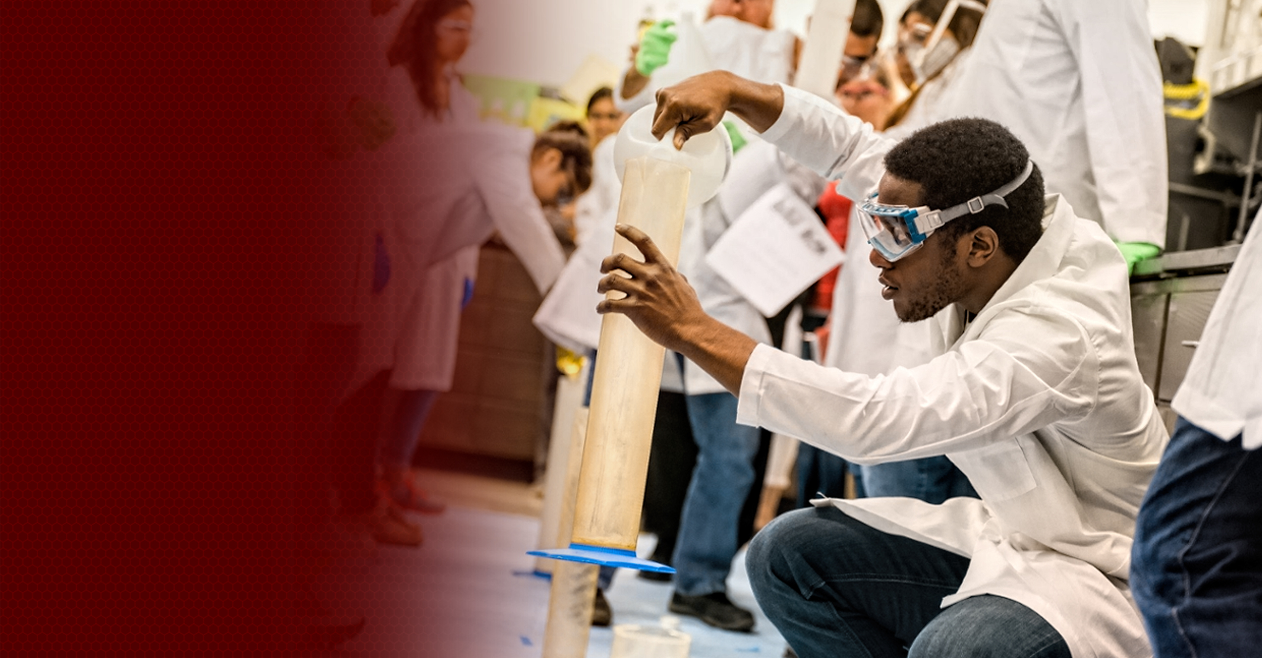 A person in safety goggles conducting a science experiment at a bustling educational event, demonstrating a chemical reaction in a large test tube.