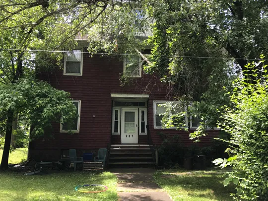 A red brick house with white windows, a white door, a lawn of green grass, and trees in the yard.