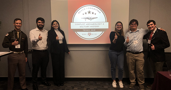 Students at the "Never Forgotten" event stand in front of the event logo