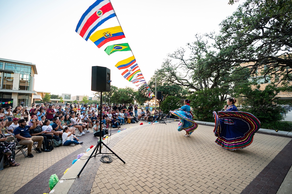 Dancers dressed in brightly colored traditional dresses show off their skills in front of a large crowd at Rudder Plaza on the Texas A&M University campus
