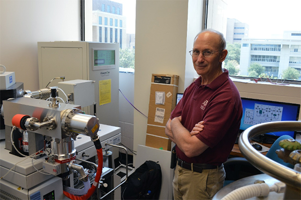 Texas A&M geologist Ethan Grossman stands next to a mass spectrometer in his laboratory on the Texas A&M University campus