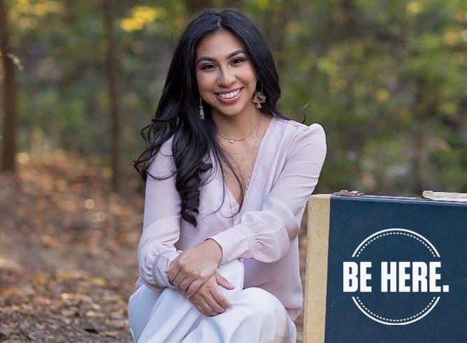 Texas A&amp;M women's and gender studies major Odyssey Olmos smiles for the camera while sitting beside two suitcases in a tree-lined background setting