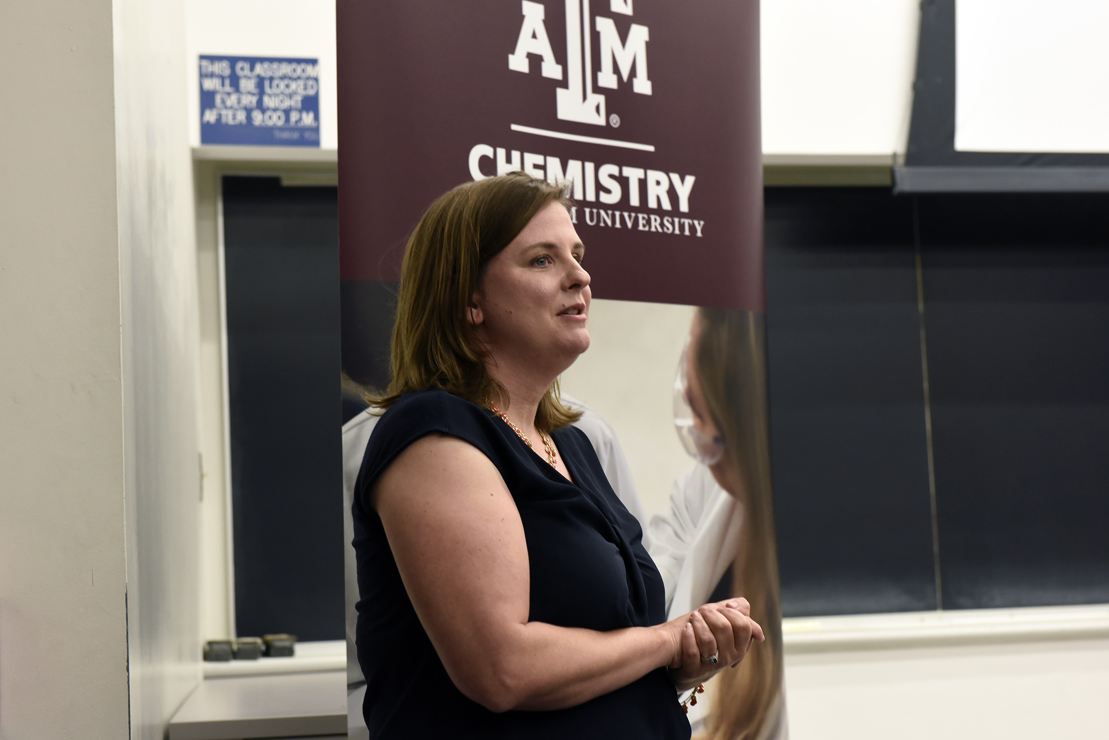 Texas A&amp;M University chemist Joanna Goodey-Pellois speaks from the front of a classroom with a Texas A&amp;M Chemistry banner and chalkboards in the background