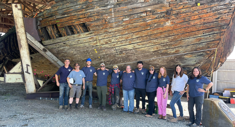 Group photo of the Texas A&amp;M University nautical archaeology team standing in front of the Equator in dry dock in Everett, Washington, in 2023