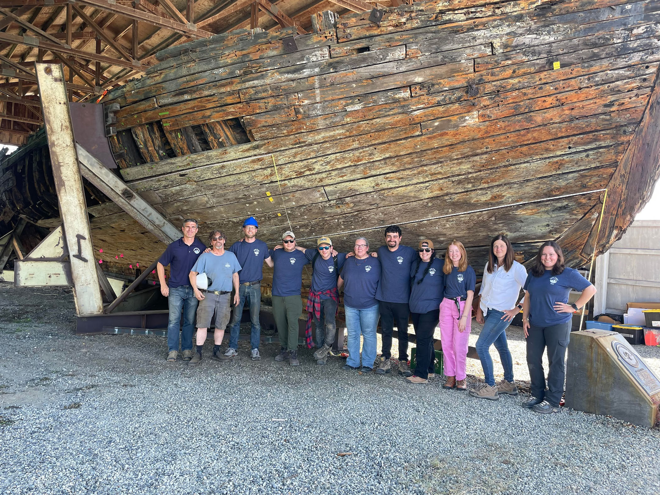 Group photo of the Texas A&amp;M University nautical archaeology team standing in front of the Equator in dry dock in Everett, Washington, in 2023