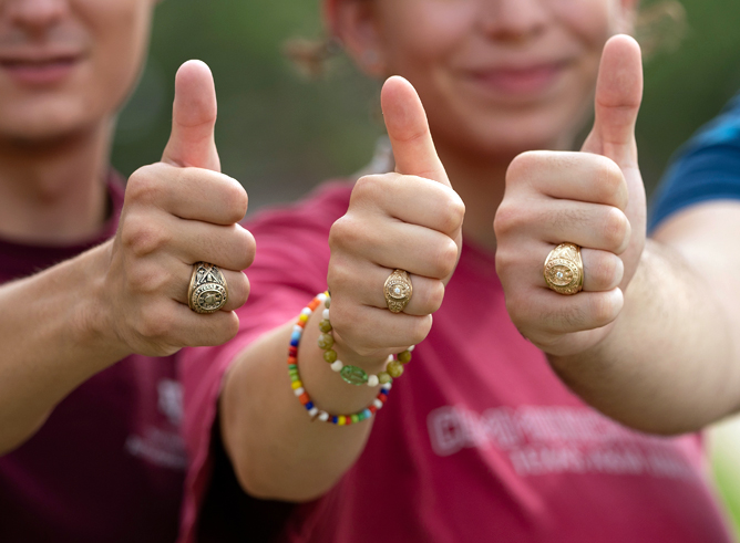Close-up of three Texas A&M University students flashing gig 'ems for the camera with their Aggie Rings prominently displayed