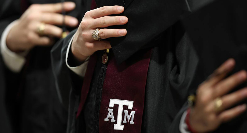 Close-up of Texas A&M University graduates in regalia, holding their mortar boards with their Aggie Rings and maroon stoles featuring the white aTm logo visible