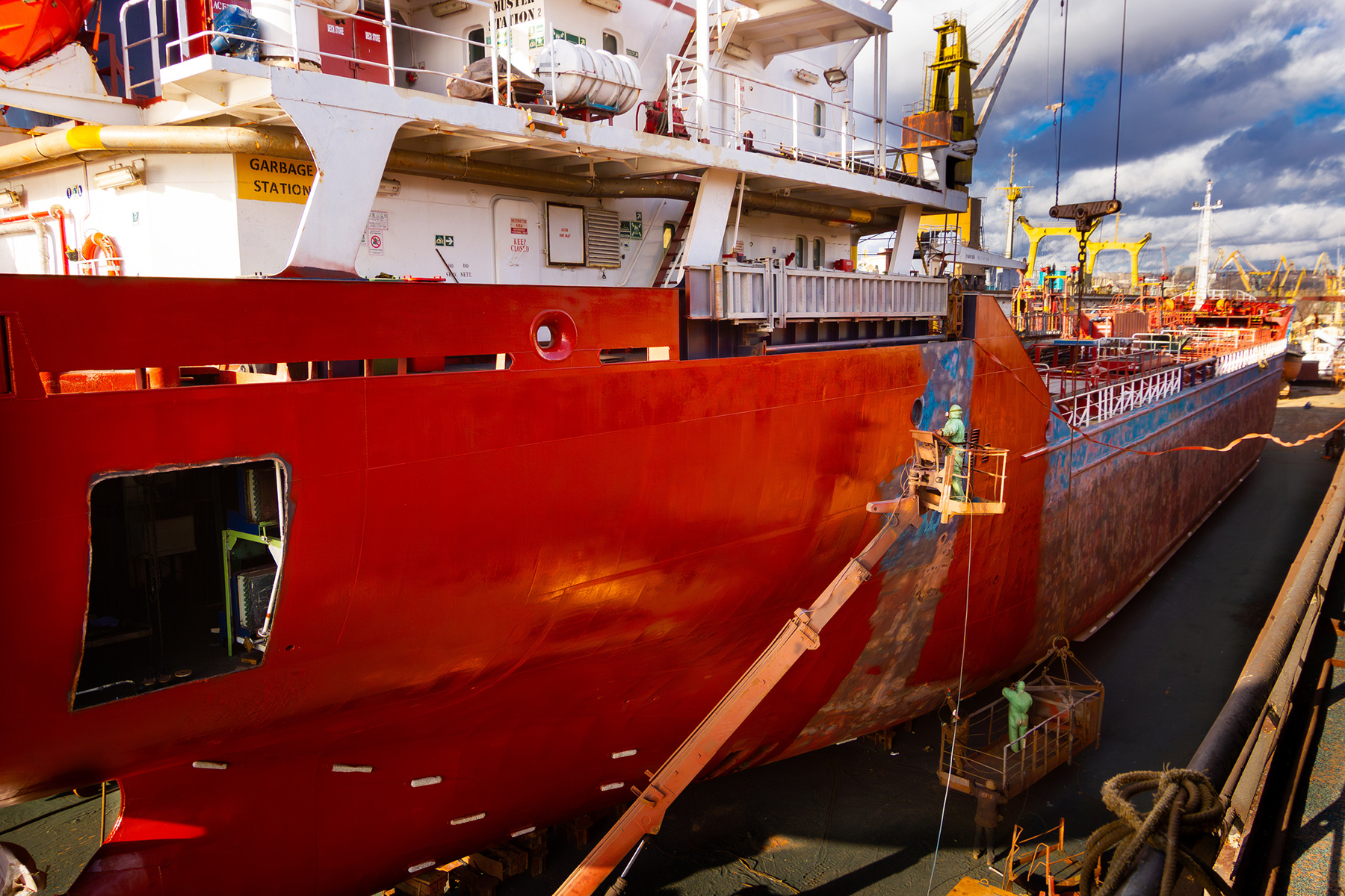 Workers paint and repair a ship's hull while it is undergoing maintenance in a floating dock