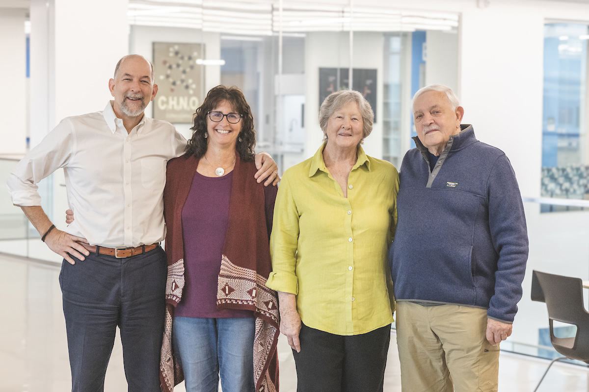 Four people posing with smiles in an office setting with a sign that reads "CHNO" in the background.