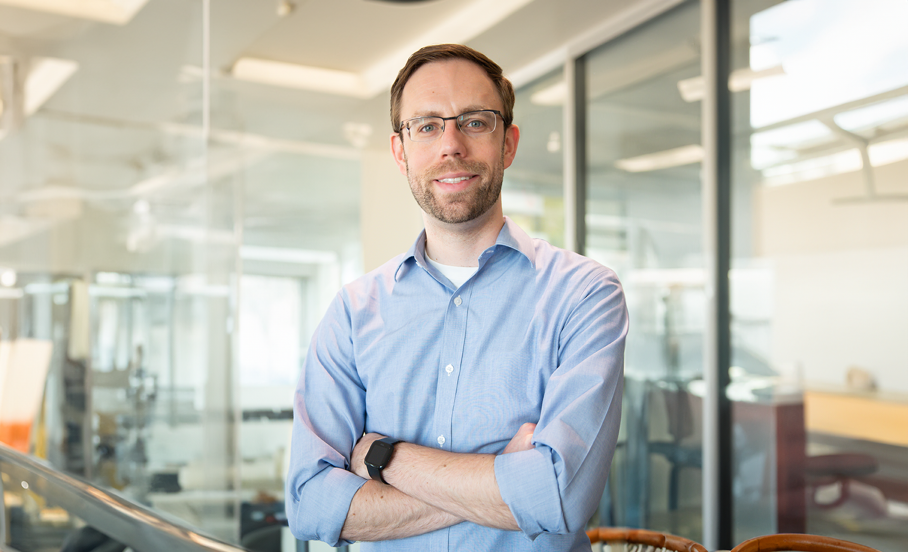 A smiling Dawson Nodurft stands in front of a glass wall with his arms crossed 