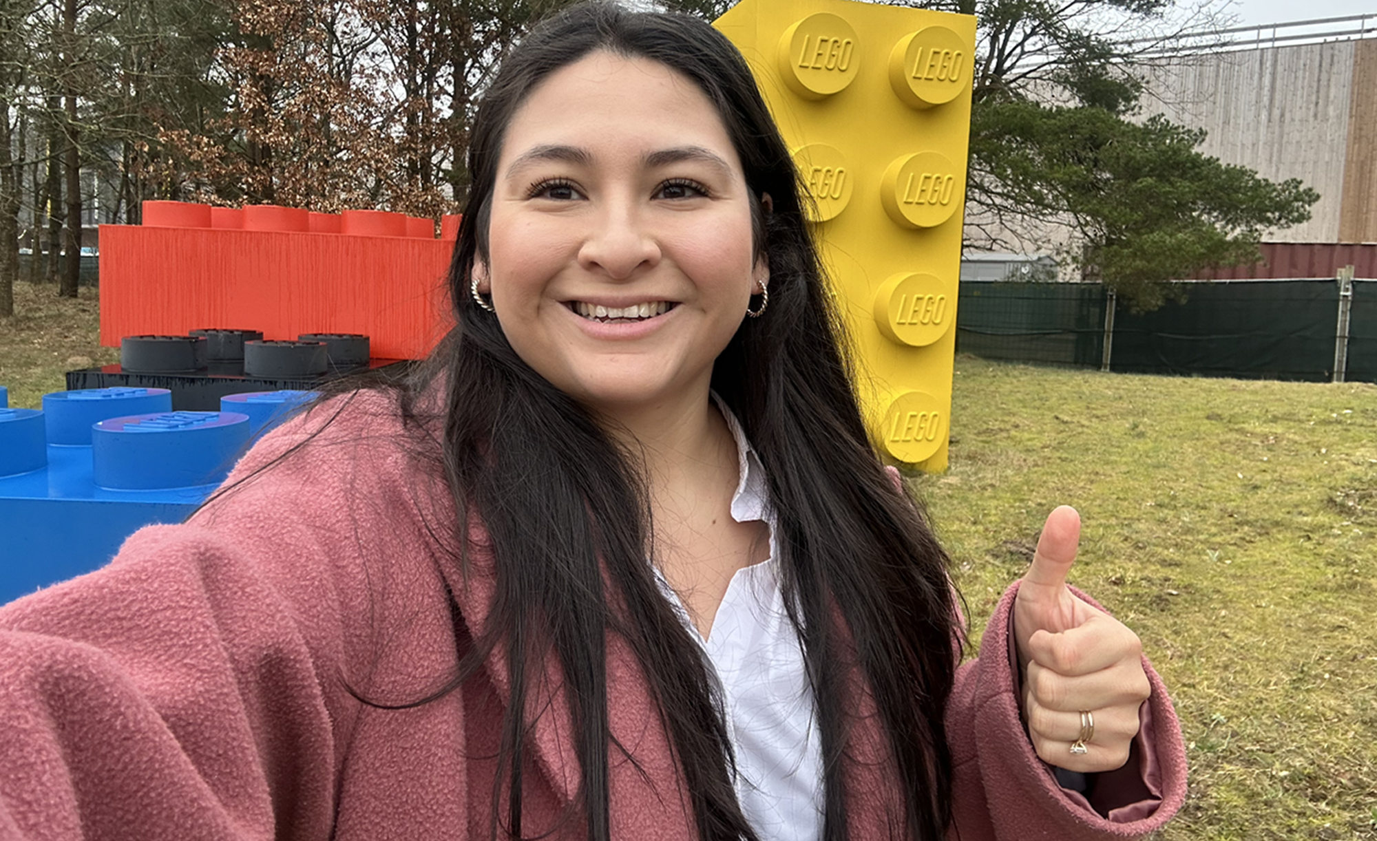 Jennifer Chavez smiling with a thumbs up in front of large LEGO bricks.