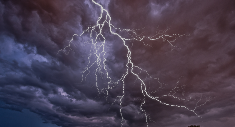 Lightning striking over a landscape with mountains and houses under a dramatic cloudy sky.