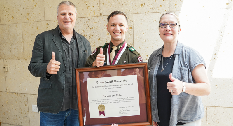 Dr. Darryl De Ruiter, Jackson Baker, and  Dr. Angela P. Hudson pose for a photo, with Baker holding a framed award certificate. All three are giving a thumbs-up.