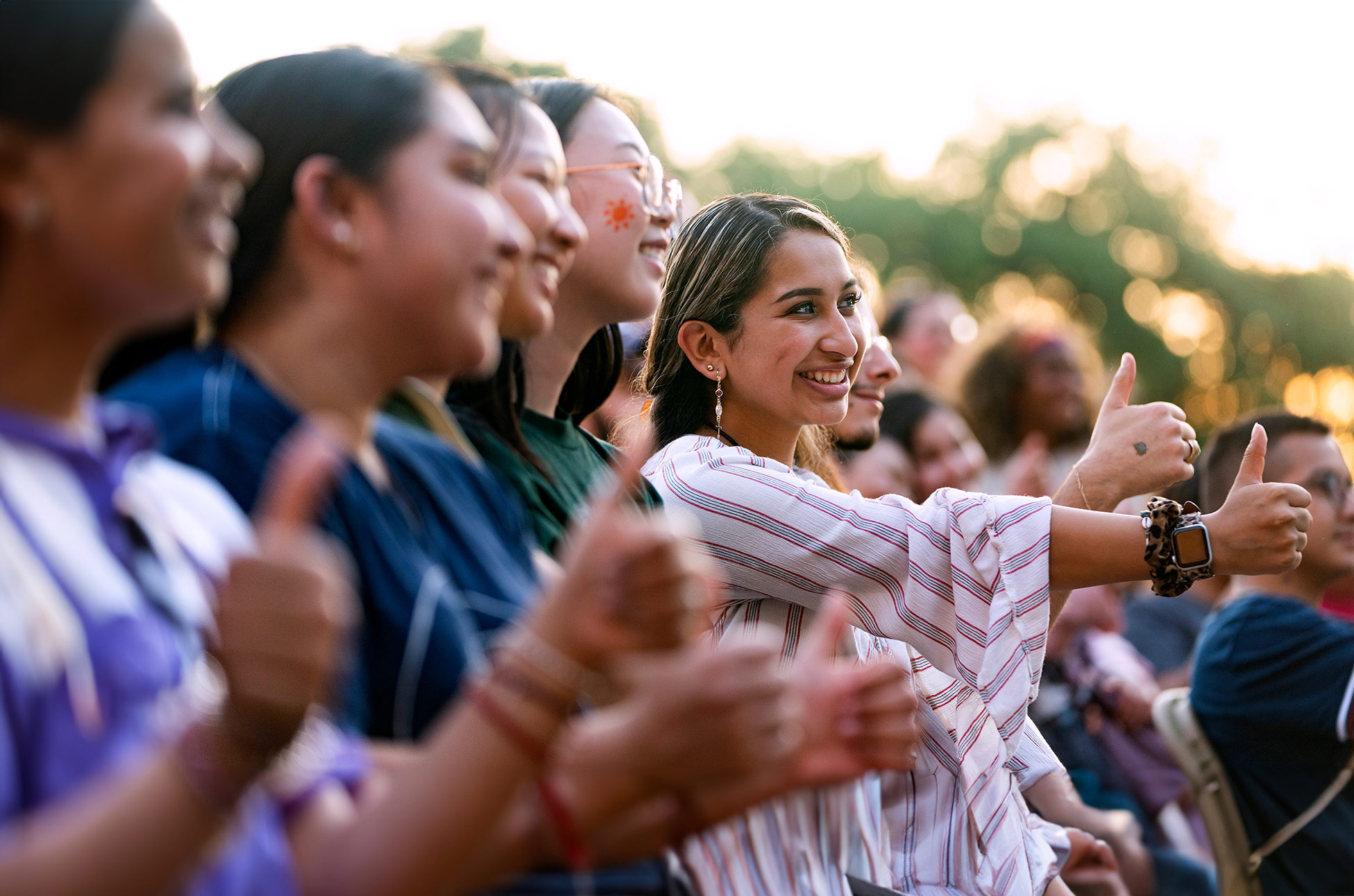 young woman smiling and holding out a thumbs up among group of people